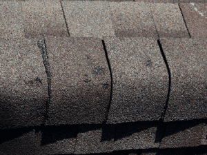 Damaged roof shingles with cracks and lifting on a roof in Georgia.