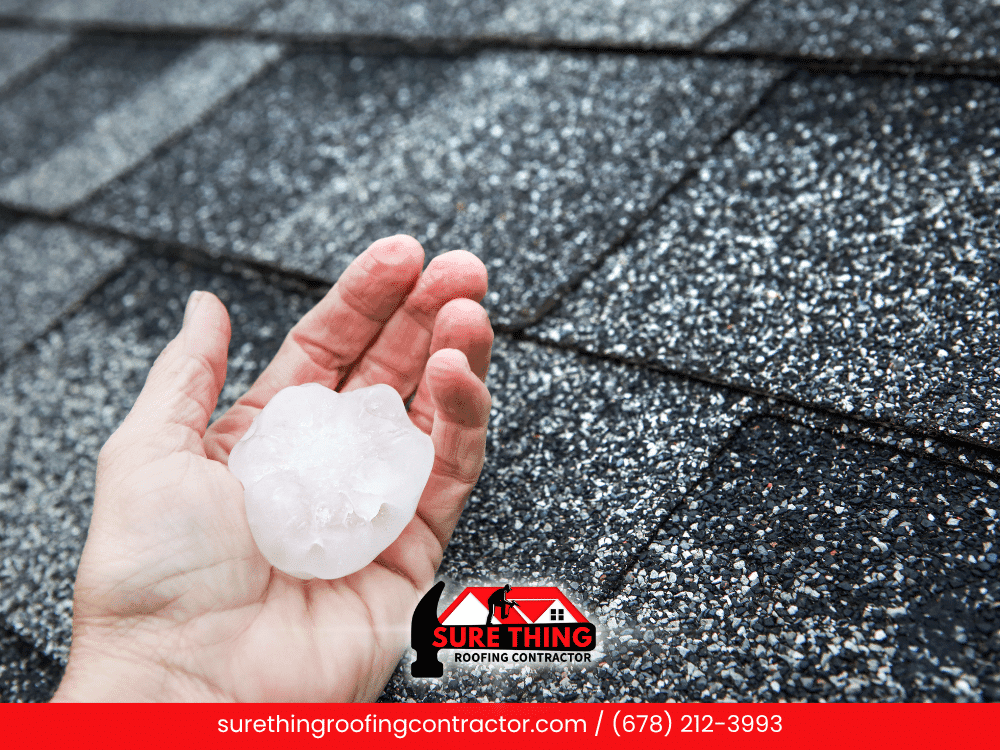 Hand holding large hail with damaged roof shingles in Georgia.